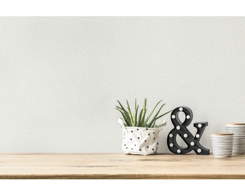 Papier peint intissé blanc texturé sur un mur au-dessus d'une table en bois clair avec une plante et des éléments décoratifs.