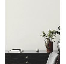 Papier peint blanc structuré sur un mur derrière un bureau sombre avec des objets de décoration.
