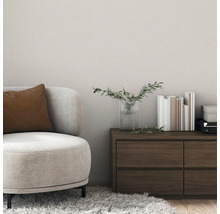 Salon moderne avec revêtement mural texturé, fauteuil beige avec coussin marron et commode en bois foncé.