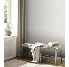 Papier peint intissé gris clair avec aspect crépi fin sur le mur d'un salon lumineux avec banc en bois et fenêtre.