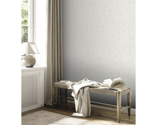 Papier peint intissé gris clair avec aspect crépi fin sur le mur d'un salon lumineux avec banc en bois et fenêtre.