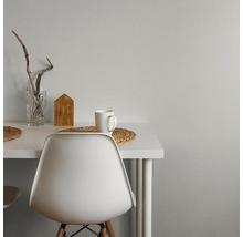 Espace de travail moderne avec bureau et chaise blancs contre un mur gris texturé. Décoré d'un vase en verre, d'une décoration en bois et d'une tasse.