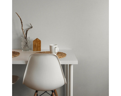 Espace de travail moderne avec bureau et chaise blancs contre un mur gris texturé. Décoré d'un vase en verre, d'une décoration en bois et d'une tasse.