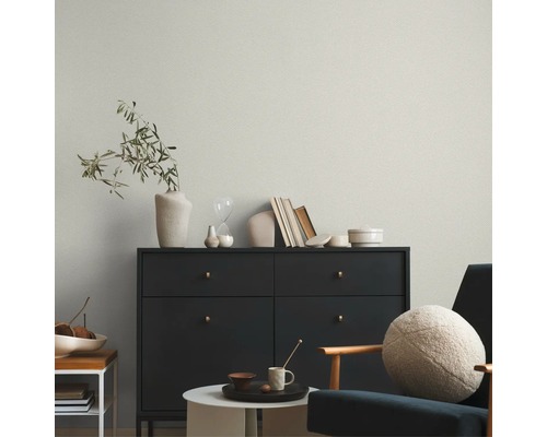 Papier peint intissé clair avec structure fine derrière une commode sombre dans un salon au design moderne.