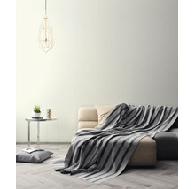Salon lumineux avec mur crème, canapé avec couverture rayée, table d'appoint et suspension géométrique sur parquet.