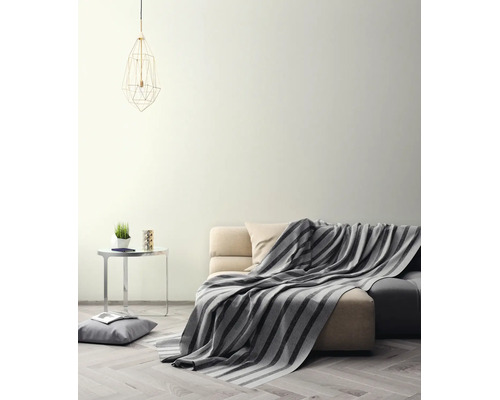 Salon lumineux avec mur crème, canapé avec couverture rayée, table d'appoint et suspension géométrique sur parquet.
