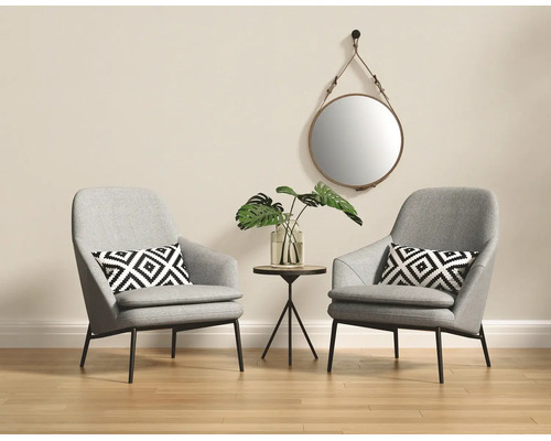Salon lumineux avec deux fauteuils gris, coussins à motifs géométriques, une petite table d'appoint ronde et un miroir mural rond.