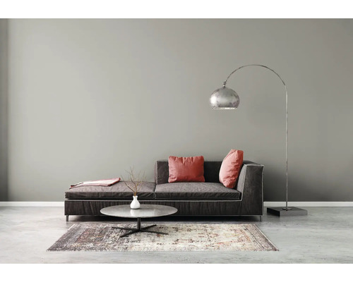Salon moderne avec canapé en tissu foncé, coussins rouges, table basse ronde en marbre, tapis à motifs et lampadaire à arc argenté.