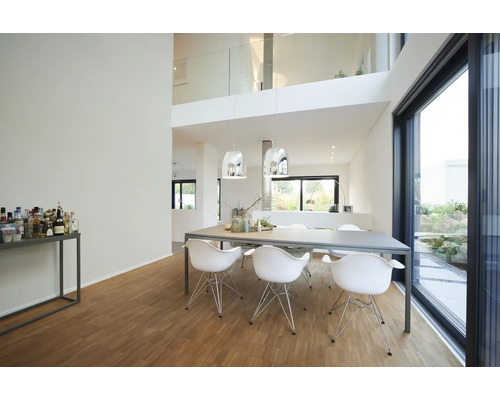 Salle à manger moderne et lumineuse avec table grise, chaises blanches, parquet en bois et grandes baies vitrées.