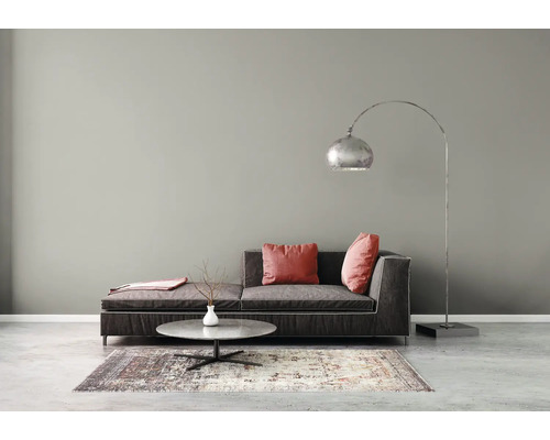 Salon moderne avec canapé gris foncé, lampadaire arqué, table basse ronde et tapis à motifs contre un mur gris.