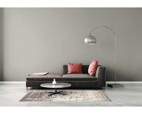 Salon moderne avec mur gris, canapé gris foncé, coussins rouges, lampadaire arc argenté et table basse ronde sur un tapis à motifs.