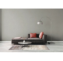 Salon moderne avec canapé foncé, coussins roses, table basse ronde en pierre, lampadaire à arc argenté et tapis à motifs devant un mur gris.
