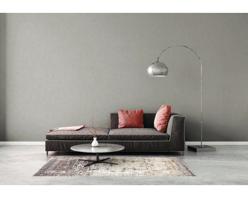 Salon moderne avec canapé foncé, coussins roses, table basse ronde en pierre, lampadaire à arc argenté et tapis à motifs devant un mur gris.