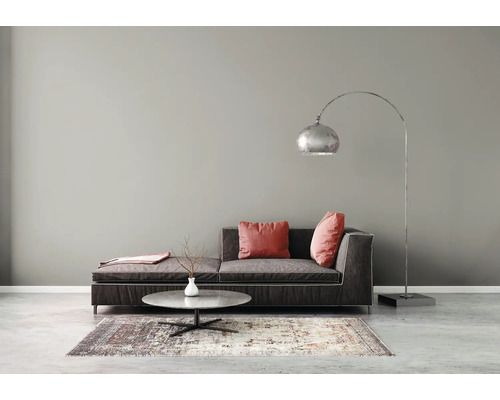 Salon moderne avec peinture murale grise, canapé en tissu foncé, table basse ronde, tapis à motifs et un grand lampadaire arqué en métal.