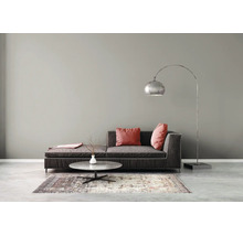Salon moderne avec canapé gris foncé, coussins rouges, lampadaire arqué argenté, table basse ronde et tapis à motifs contre un mur gris.