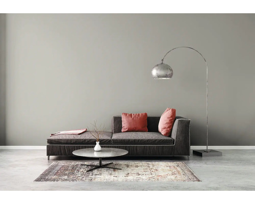 Salon moderne avec peinture murale grise, canapé sombre avec coussins rouges, table basse ronde, tapis à motifs et lampadaire à arc.