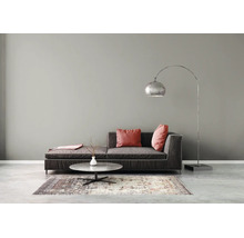 Salon minimaliste avec un canapé en tissu sombre, une table basse ronde en pierre sur un tapis et un grand lampadaire arqué en métal.