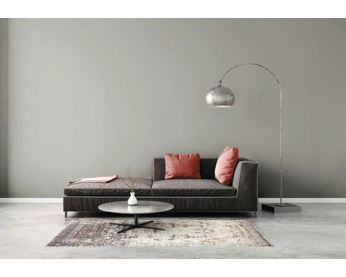 Salon minimaliste avec un canapé en tissu sombre, une table basse ronde en pierre sur un tapis et un grand lampadaire arqué en métal.