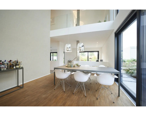 Salle à manger moderne et lumineuse avec grande table grise, chaises design blanches, suspensions chromées et parquet devant une baie vitrée.