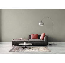 Salon moderne avec mur gris texturé, canapé gris foncé, coussins roses, table basse et un grand lampadaire arqué en métal.