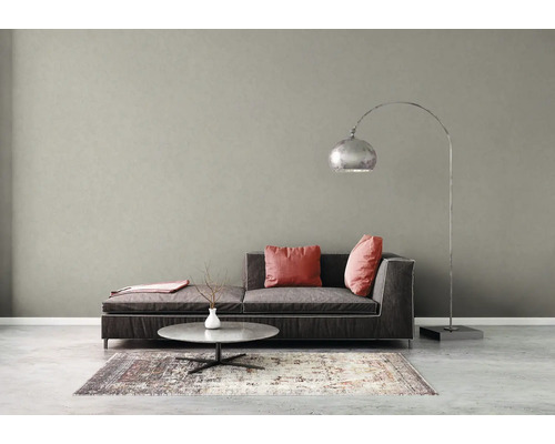 Salon moderne avec mur gris texturé, canapé gris foncé, coussins roses, table basse et un grand lampadaire arqué en métal.