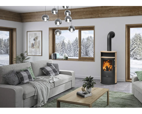 Moderner Kaminofen mit Feuer in hellem Wohnzimmer mit grauem Sofa, Holztisch und Blick auf verschneite Waldlandschaft.