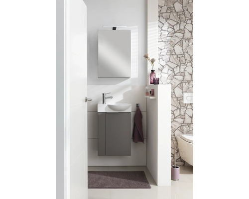 Ensemble de toilettes pour invités moderne avec meuble sous lavabo gris, lavabo blanc, miroir avec éclairage et mur en pierre naturelle.
