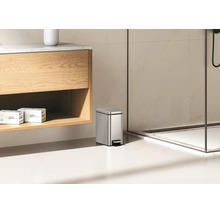 Poubelle à pédale rectangulaire en acier inoxydable dans une salle de bain moderne à côté d'un meuble sous vasque.