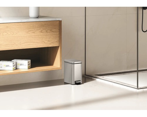 Poubelle à pédale rectangulaire en acier inoxydable dans une salle de bain moderne à côté d'un meuble sous vasque.
