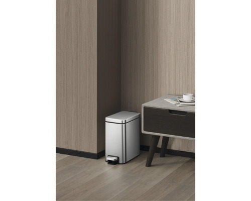 Poubelle à pédale rectangulaire en acier inoxydable dans une pièce moderne avec des parois en bois à côté d'une table.