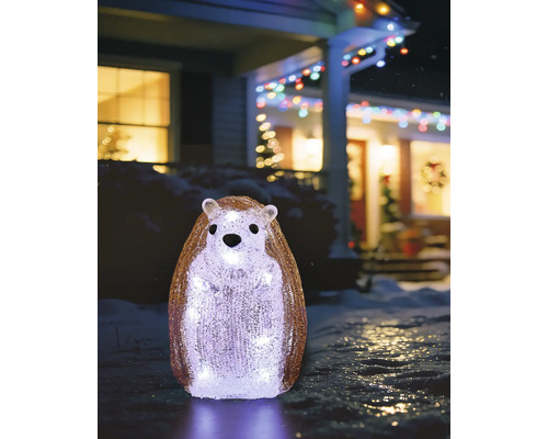Hérisson debout en acrylique, éclairé en blanc froid, décoration hivernale dans un jardin enneigé devant une maison illuminée.