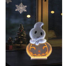 Décoration d'Halloween LED fantôme sur citrouille avec effet miroir infini devant une fenêtre à côté d'un sapin de Noël décoré.