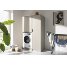 Armoire pour lave-linge beige avec colonne dans une buanderie lumineuse avec séchoir et paniers à linge.