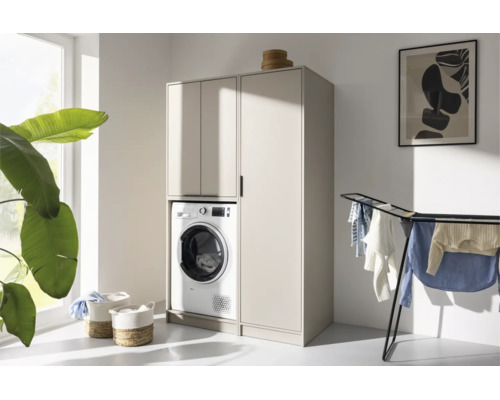 Armoire pour lave-linge beige avec colonne dans une buanderie lumineuse avec séchoir et paniers à linge.