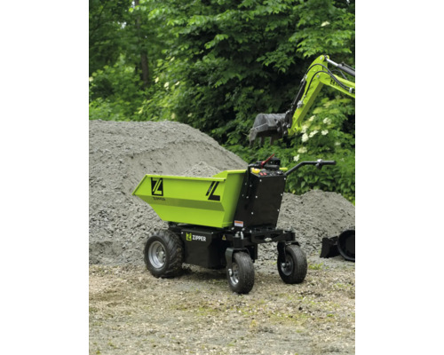 Brouette électrique Zipper sur un chantier à côté d'un tas de sable et d'un bras de pelle.