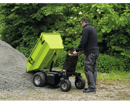 Un homme vide un dumper motorisé Zipper avec mécanisme de basculement sur un tas de gravier. Environnement extérieur fonctionnel. Zipper Logo.