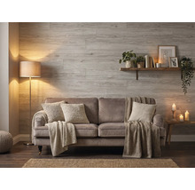Salon avec des panneaux muraux en aspect bois, un canapé avec des coussins et des couvertures, un lampadaire et une étagère murale.