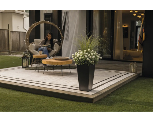 Terrasse moderne avec tapis d'extérieur, tables en bois rondes, un fauteuil suspendu et un pot de fleurs haut avec des fleurs et des herbes.