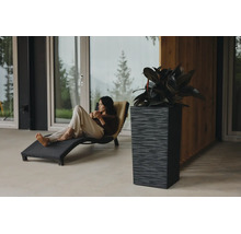 Jardinière rectangulaire haute et structurée avec plante sur une terrasse moderne à côté d une femme sur une chaise longue noire.