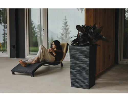 Jardinière rectangulaire haute et structurée avec plante sur une terrasse moderne à côté d une femme sur une chaise longue noire.