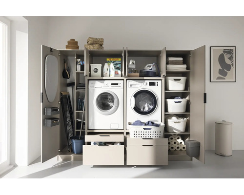 Organisierter Waschmaschinenschrank mit Waschmaschine, Trockner, Regalfächern, Schubladen und Platz für Bügelbrett und Waschmittel.