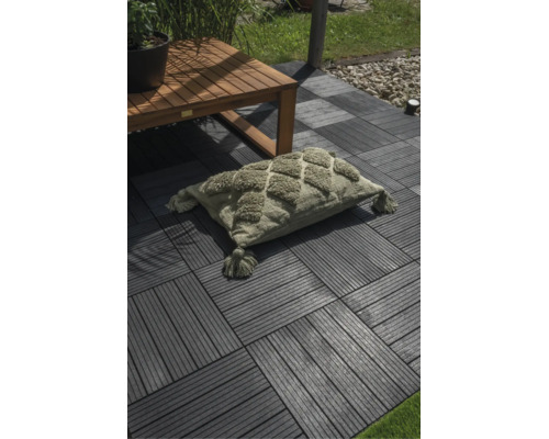 Rechteckiges Kissen mit getuftetem Rautenmuster und Quasten auf einer Terrasse mit Klickfliesen und Holztisch.
