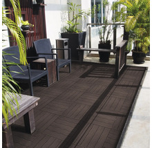 Terrasse mit dunkelbraunen WPC-Fliesen im Schachbrettmuster, möbliert mit Rattanstühlen, Holztischen und grünen Pflanzen in schwarzen Pflanzkübeln.