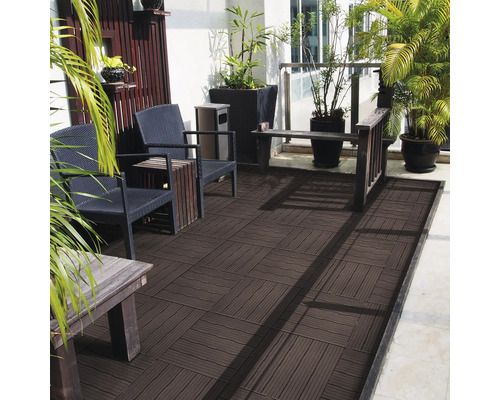Terrasse mit dunkelbraunen WPC-Fliesen im Schachbrettmuster, möbliert mit Rattanstühlen, Holztischen und grünen Pflanzen in schwarzen Pflanzkübeln.