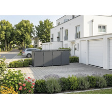 Abri pour quatre poubelles moderne en métal dans une allée pavée devant une maison blanche avec des plantations.