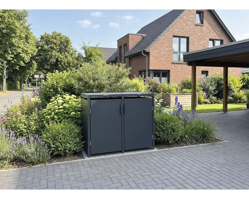 Cache-poubelle en métal gris foncé pour deux poubelles dans un jardin fleuri à côté d'une allée pavée.