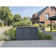 Abri triple moderne pour poubelles en métal dans un jardin devant une maison en briques.