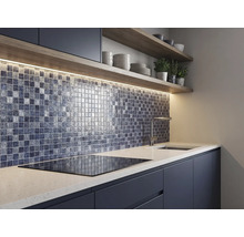 Cuisine moderne avec une crédence en mosaïque de verre, éclairage sous les meubles, étagères en bois et plan de travail blanc avec plaque de cuisson.