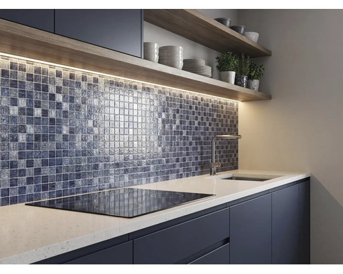 Cuisine moderne avec une crédence en mosaïque de verre, éclairage sous les meubles, étagères en bois et plan de travail blanc avec plaque de cuisson.