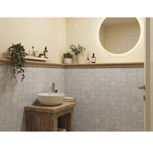Salle de bains moderne avec miroir rond éclairé, vasque blanche sur meuble en bois rustique et carrelage mural carré gris.
